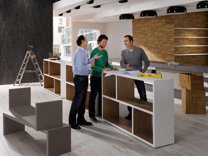 Planungsgespräch für Messe-/Showroomaufbau Planungsgespräch für Messe-/Showroomaufbau zwischen drei Männern mit unfertigen Mobiliar im Hintergrund